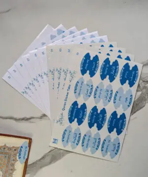 Quran sticker tabs by Iman & Ink Store, sheets of light and dark blue surah tabs fanned out, with an Al-Fatihah tab on a Quran page